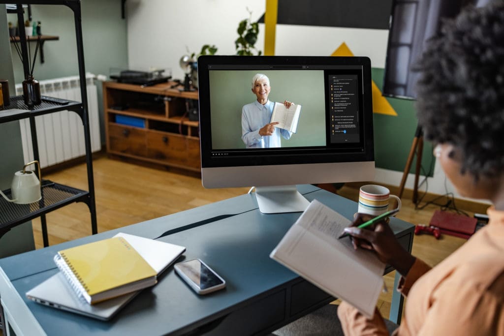 Young woman writing notes while watching video lesson on her computer.